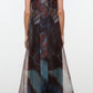 A person wearing the Staud Albee Dress—an organza, sleeveless, floor-length gown with a multicolored geometric pattern and a keyhole back design, complete with an interior slip for added comfort—stands against a plain background.