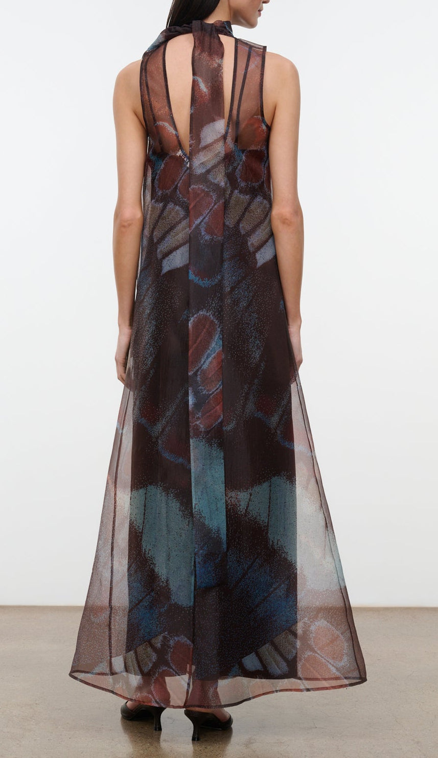 A person wearing the Staud Albee Dress—an organza, sleeveless, floor-length gown with a multicolored geometric pattern and a keyhole back design, complete with an interior slip for added comfort—stands against a plain background.