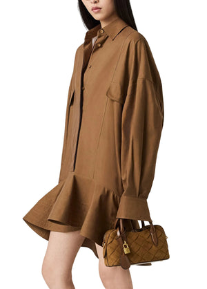 A woman wears the Stella McCartney Washed Cotton Peplum Shirt Dress in brown and holds a small quilted brown handbag with a lock detail.