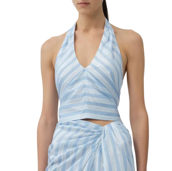 A woman is shown from shoulders to hips wearing the Simkhai Caprie Halter Top in Oxford Blue and white satin stripes, paired with a matching wrap skirt.