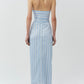 A woman stands with her back to the camera, wearing the Simkhai Caprie Halter Top in Oxford Blue and white stripes, paired with white strappy heels against a plain light background.