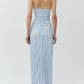 A woman faces away, wearing the Simkhai Liorra Draped Midi Skirt—a light blue and white striped wrap-effect skirt with a back tie—styled with white strappy heels.