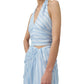 A woman models the Simkhai Caprie Halter Top in light blue and white satin stripes, paired with a matching wrap skirt. The image is cropped from shoulders to mid-thigh against a white background.