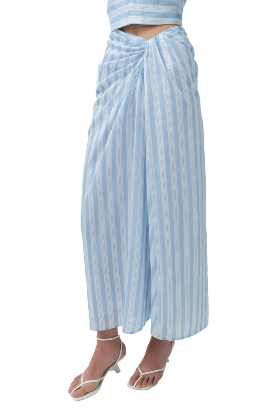 Lower body shown wearing the Simkhai Liorra Draped Midi Skirt in oxford blue, paired with white heeled sandals and a coordinating cropped top.