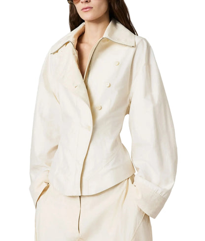 A woman wears the Stella McCartney Washed Cotton Utility Top, a cream double-breasted jacket with wide lapels and matching pants, accessorized with sunglasses and her long brown hair.