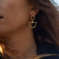 Close-up of a person in a blue garment with long brown hair, wearing Anabel Aram's Cheval Bit Drop Earrings and a matching gold necklace.