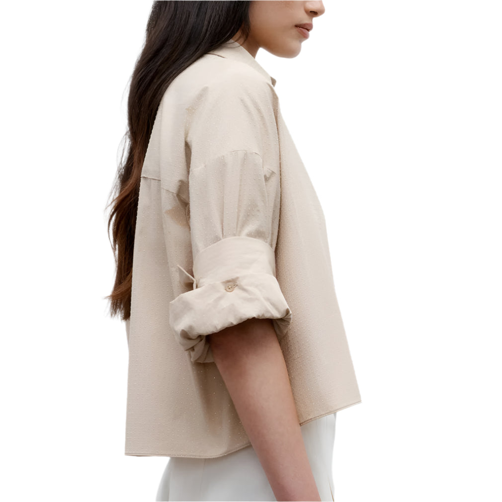 A woman is shown from the side wearing the TWP Next Ex Crystal Shirt, a cropped superfine cotton button-down with rolled sleeves, paired with white pants against a plain white background.