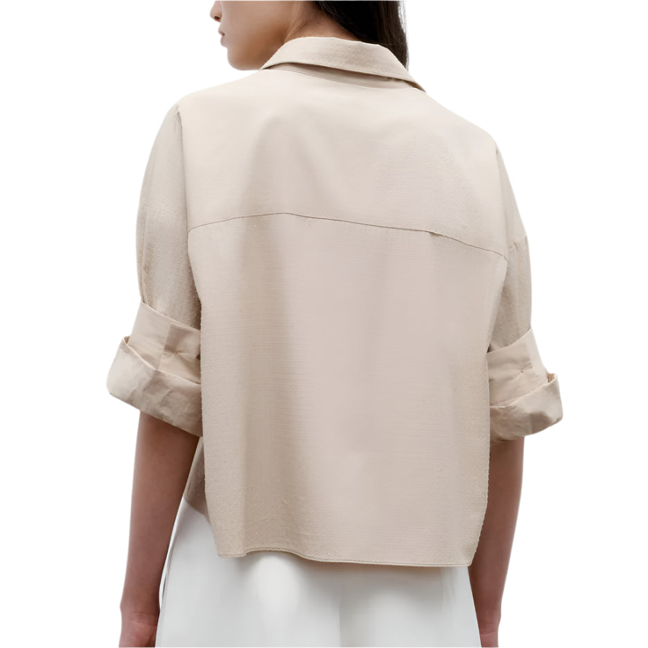 A person wearing the TWP Next Ex Crystal Shirt—a light beige, superfine cotton, collared, long-sleeve shirt with rolled cuffs—seen from the back against a plain white background.