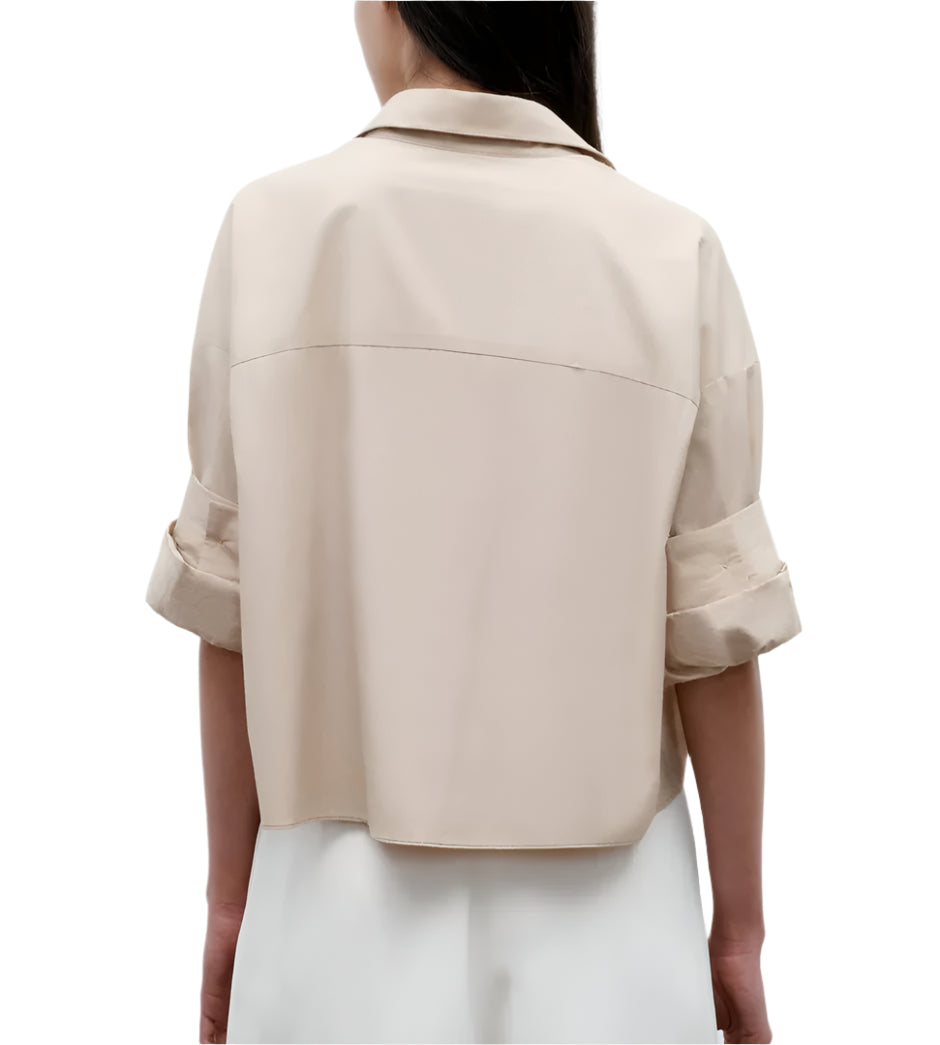 A woman is seen from the back wearing TWP's Next Ex Vintage Washed Poplin, a loose-fitting, collared shirt with rolled-up sleeves, paired with white pants.