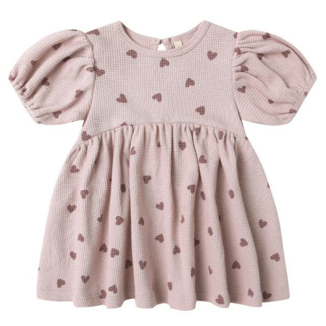 The Quincy Mae Baby Girls' and Girls' Darla Dress features a pink waffle knit, short puff sleeves, an empire waist, and a brown heart pattern, shown flat on a white background.