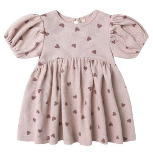 The Quincy Mae Baby Girls' and Girls' Darla Dress features a pink waffle knit, short puff sleeves, an empire waist, and a brown heart pattern, shown flat on a white background.