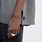 A person wearing a gray Maria McManus Cocoon Cape crafted from an alpaca-wool blend with side button detail, paired with black pants and a silver ring.