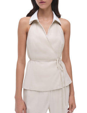 A woman wears the Simkhai Campbell Halter Shirt in ivory, a sleeveless collared wrap top with side tie and sculpted fit, paired with matching ivory pants.