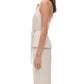 A woman stands in profile against a white background, wearing the Simkhai Campbell Halter Shirt—a sculpted fit, sleeveless beige top with a tie waist—paired with matching beige pants.