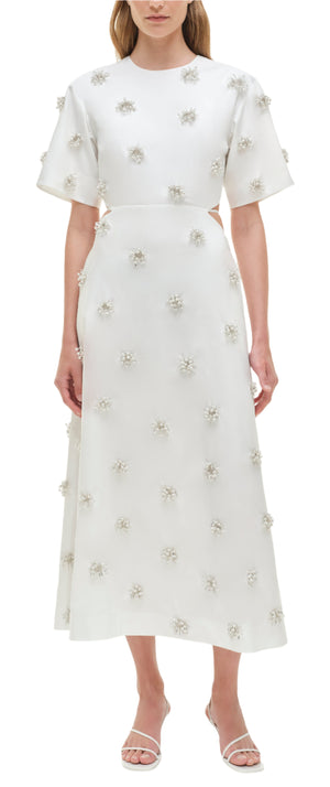A woman wears the Simkhai Starla Embellished Midi Dress, featuring oversized short sleeves, pearl and bead accents, paired with white strappy sandals.