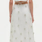 A woman faces away in the Simkhai Starla Embellished Midi Dress—white cotton poplin with textured floral details and a cinched waist—paired with white sandals.