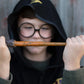 A child dressed in a black hooded robe and round glasses holds the Great Pretenders Wizard Wand horizontally in front of their face, making it the perfect kids costume accessory.