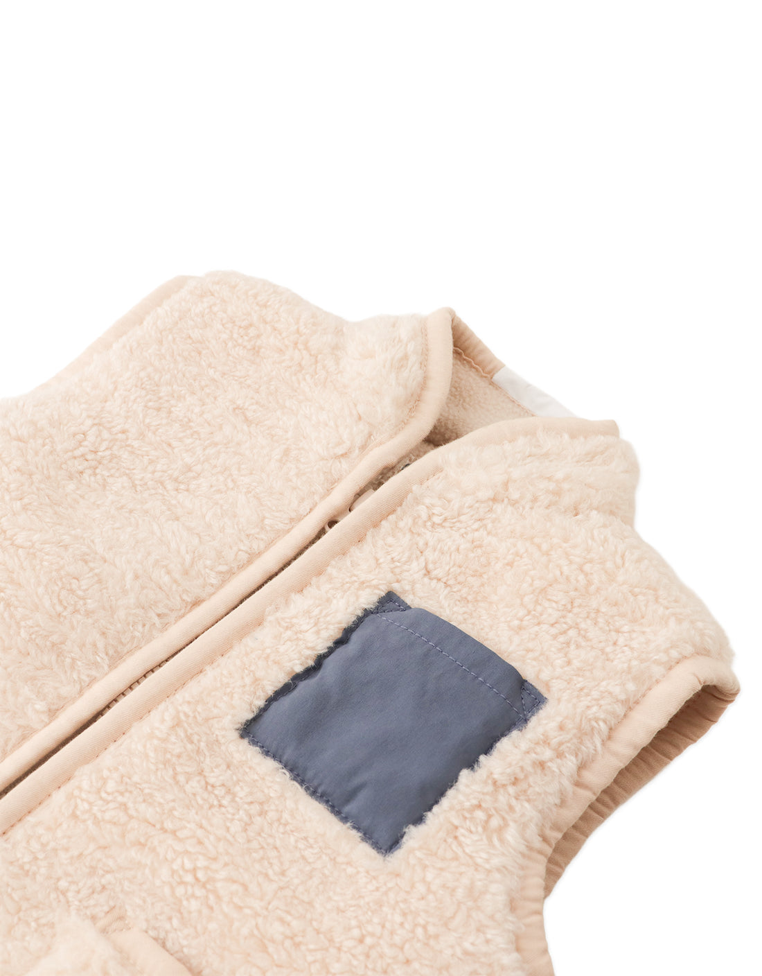 The Baby Orazio Sherpa Vest by Gingersnaps features soft, textured beige fleece, a front zipper, and a navy blue rectangular patch on the left side—making it an ideal plush sherpa gilet for cozy layering.