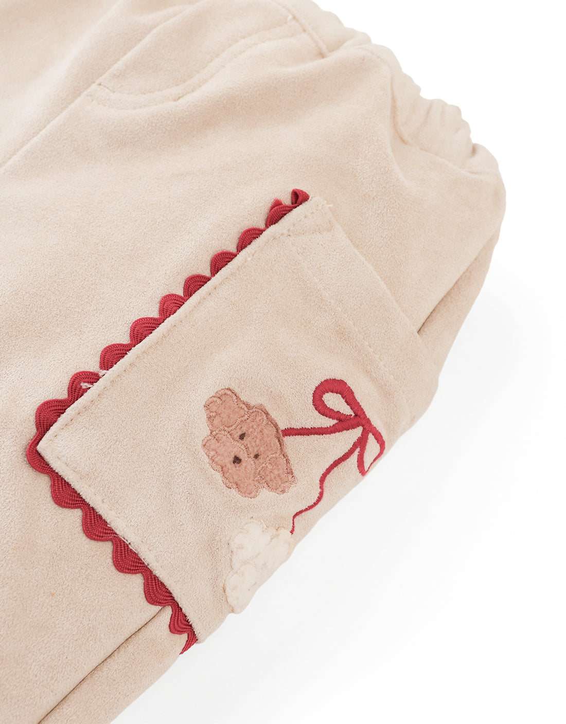 A close-up of the Baby Girls’ Nellie Pant with Poodle Pocket by Gingersnaps shows beige fabric pants with an elastic waistband, playful poodle-embroidered pocket accented with red trim, and comfy straight-leg styling for charming everyday wear.