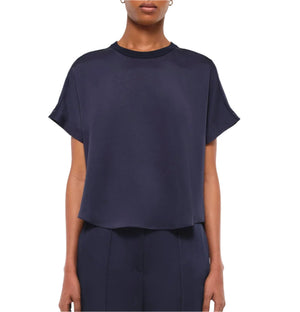 A person wears the Simkhai Addy Satin T-Shirt, featuring a relaxed fit, short sleeves, and a round neckline in navy blue, paired with matching pants, shown waist up against a plain background.