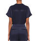 A woman is seen from behind wearing the Simkhai Addy Satin T-Shirt in navy, featuring a relaxed fit and short sleeves, paired with matching navy pants with welt pockets, set against a plain white background.