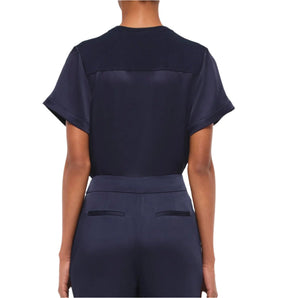A woman is seen from behind wearing the Simkhai Addy Satin T-Shirt in navy, featuring a relaxed fit and short sleeves, paired with matching navy pants with welt pockets, set against a plain white background.