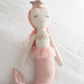 Handmade collectable Great Pretenders Melody Mermaid doll with pink hair, a tutu, and a tail, sitting against a white pillow background.