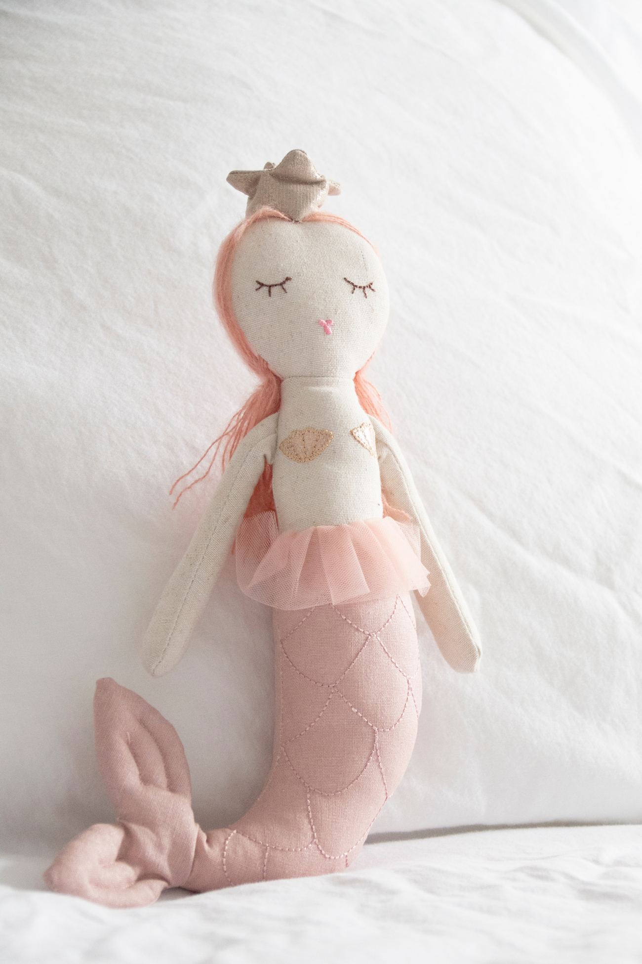 Handmade collectable Great Pretenders Melody Mermaid doll with pink hair, a tutu, and a tail, sitting against a white pillow background.