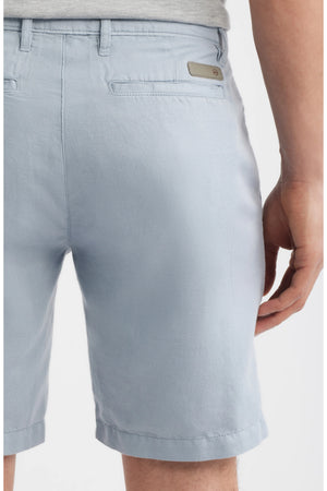 A person is shown from the back waist to above the knee wearing AG Jeans' Wanderer Shorts Linen in a light blue shade, featuring a slim cut, belt loops, and back welt pockets. One hand rests by their side, highlighting these warm weather shorts.