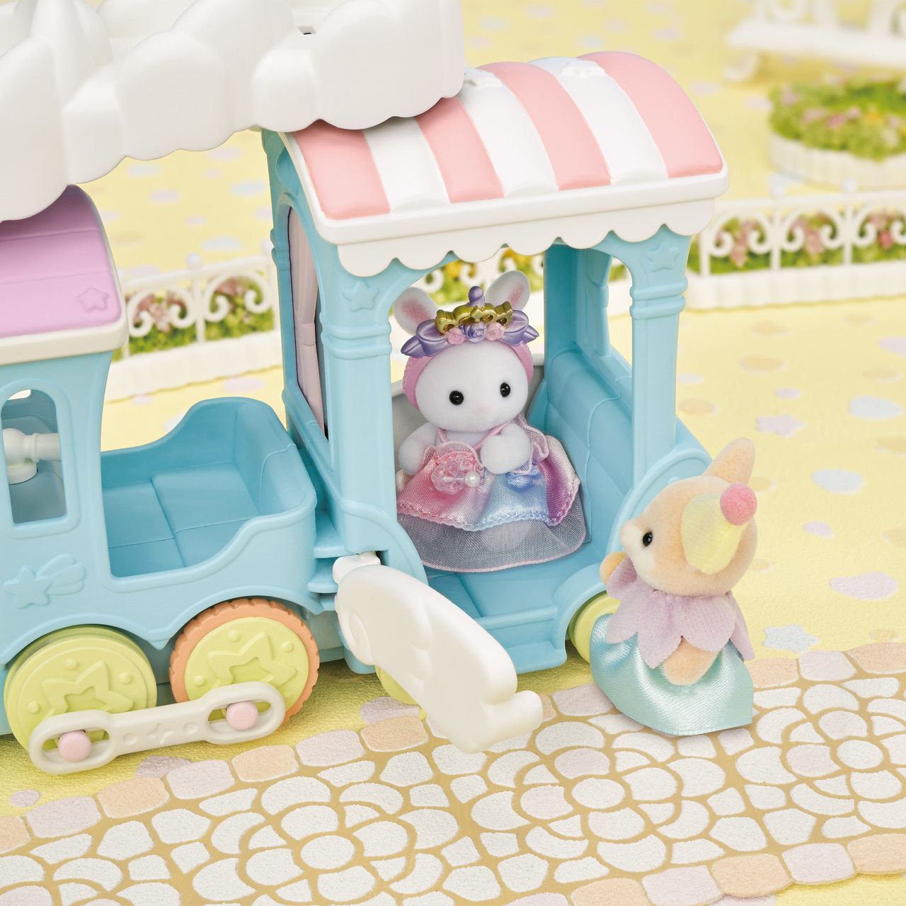 A petite Calico Critters rabbit figurine dressed in a charming outfit rides inside the pastel blue Floating Cloud Rainbow Train by Calico Critters, while a squirrel figure in a vibrant ensemble stands outside on a cheerful yellow patterned surface, evoking the playful spirit of an amusement park outing.