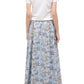 A woman facing away wears a white short-sleeve shirt, beige pointed-toe shoes, and the Staud Axel Skirt—a light blue floral pull-on maxi skirt.
