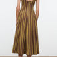 A woman stands on a plain floor facing away from the camera, wearing the Wells Midi Cotton Poplin Dress by Staud—a sleeveless design in brown and yellow stripes with a scoop back. This polished piece highlights Staud’s signature silhouette for an effortlessly refined look.