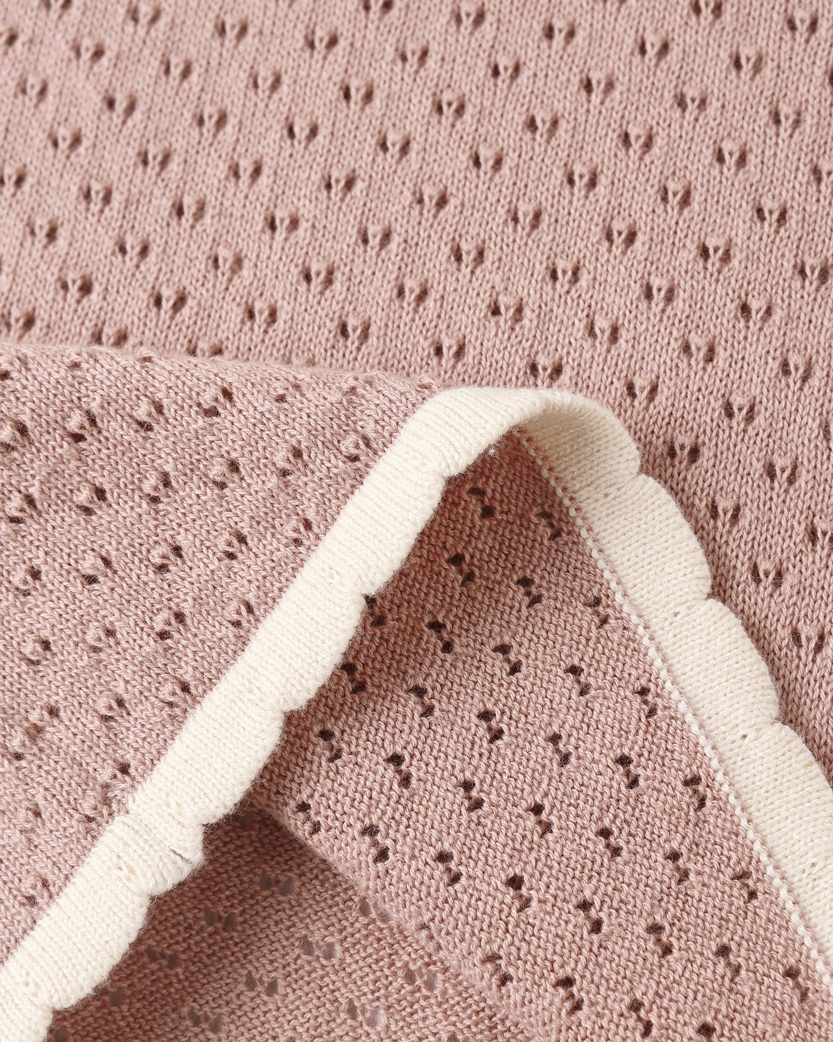 Close-up of pink perforated knit fabric with a scalloped white trim, evoking the delicate detailing found on Rylee & Cru’s Girls’ Pointelle Knit Pant, which features a scalloped hem; one corner is folded over to reveal both sides of the material.
