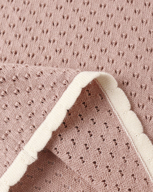 Close-up of pink perforated knit fabric with a scalloped white trim, evoking the delicate detailing found on Rylee & Cru’s Girls’ Pointelle Knit Pant, which features a scalloped hem; one corner is folded over to reveal both sides of the material.