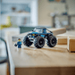 A Legos - Toyhouse LEGO® City Blue Monster Truck and a LEGO minifigure sit on a wooden table in a bright room, ready for off-road toy adventures.
