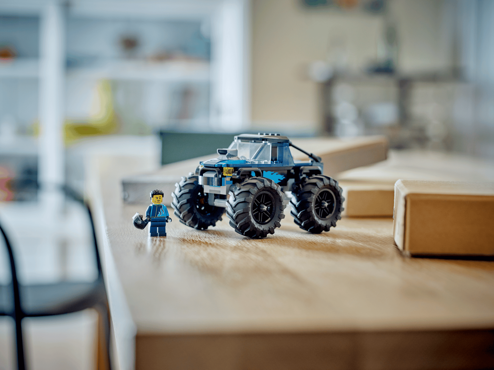 A Legos - Toyhouse LEGO® City Blue Monster Truck and a LEGO minifigure sit on a wooden table in a bright room, ready for off-road toy adventures.