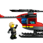 A LEGO minifigure stands beside the LEGO® City Fire Rescue Helicopter by Legos - Toyhouse, a red and black set with an open cockpit canopy and fire emblem on its tail.