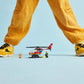 A person in yellow pants and sneakers stands with legs apart behind the LEGO® City Fire Rescue Helicopter by Legos - Toyhouse, a fireman figurine, and toy fire accessories on a light blue background.