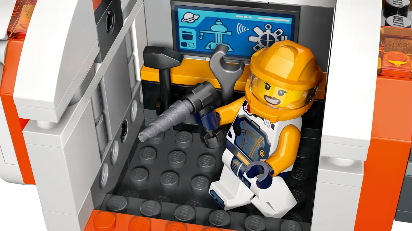 A Legos - Toyhouse LEGO® City Modular Space Station astronaut toy stands in a spacecraft, holding tools, with control panels and equipment seen behind.