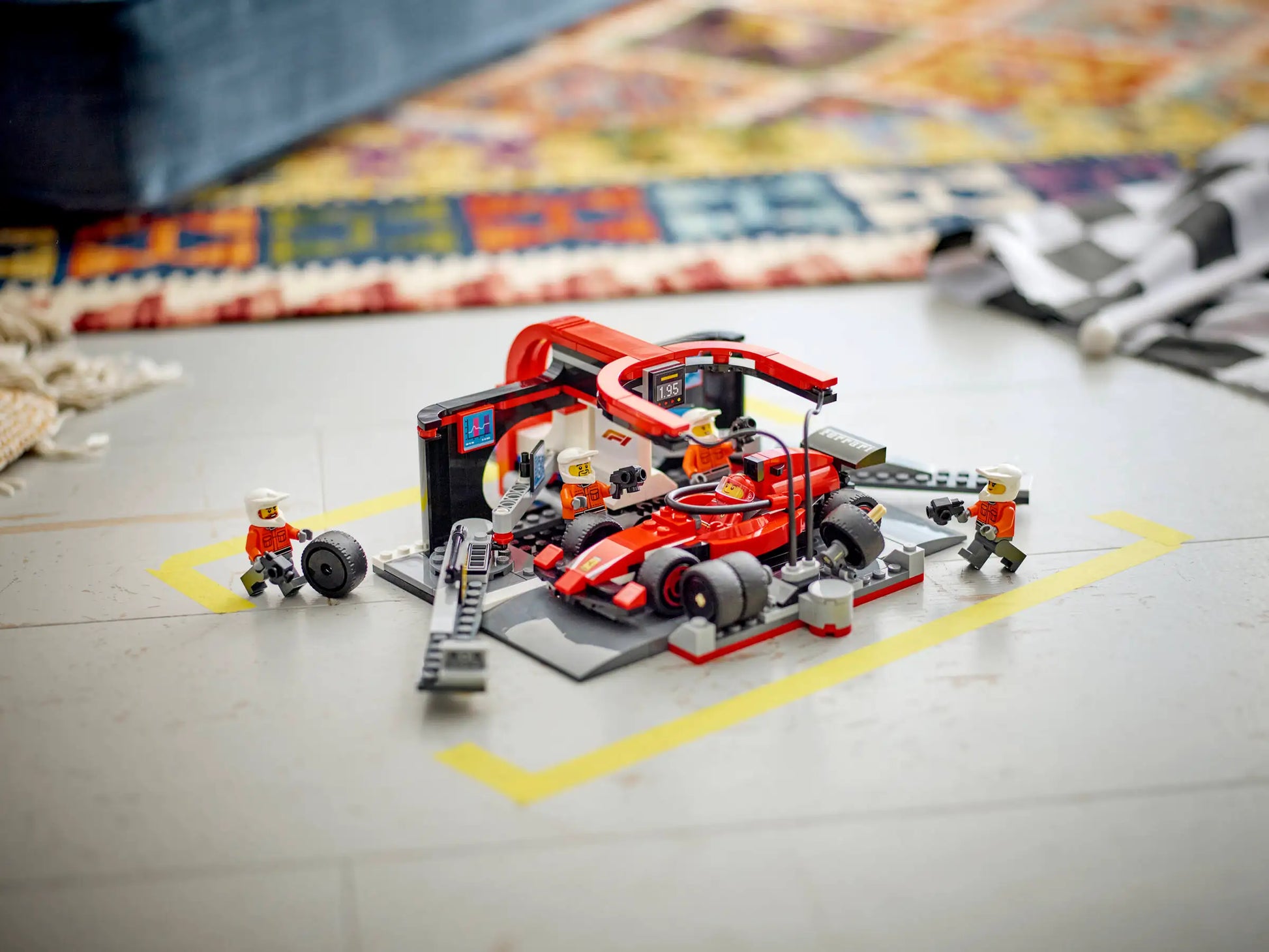 A LEGO® City F1® Pit Stop & Pit Crew with Ferrari Car by Legos - Toyhouse is set up on the floor, featuring minifigures working on a red Ferrari Formula 1 car with accessories scattered around.