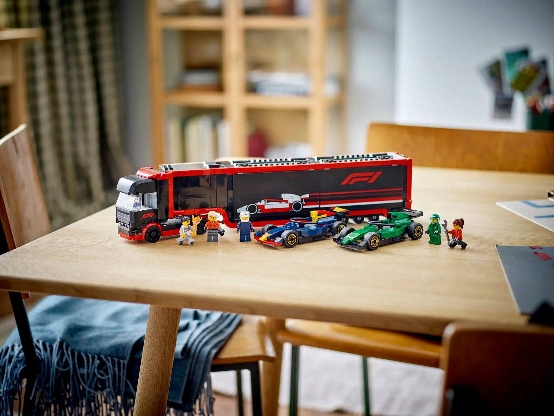 The LEGO® City F1® Truck with RB20 & AMR24 F1® Cars by Legos - Toyhouse, including Formula 1 car toys and minifigures, is displayed on a wooden table in a brightly lit room.
