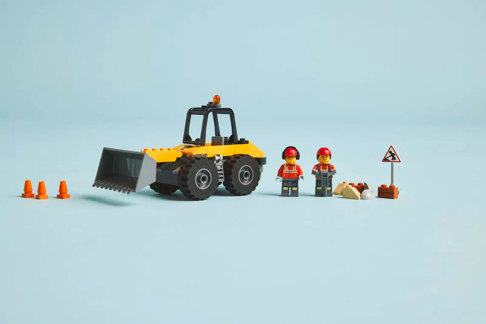 LEGO® City Yellow Construction Wheel Loader by Legos - Toyhouse includes a loader, 2 worker figures, 3 orange cones, a warning sign, and accessories on a light blue background. Ideal digger toy for young builders!.