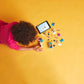 A child arranges vehicle toy parts on a yellow floor near a tablet showing images of the LEGO® City Donut Truck by Legos - Toyhouse.