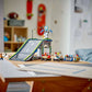 A LEGO® City No Limits: Race Car Ramp Track by Legos - Toyhouse is set up with stunt vehicles on a table in a child’s bedroom, with shelves and toys in the background.