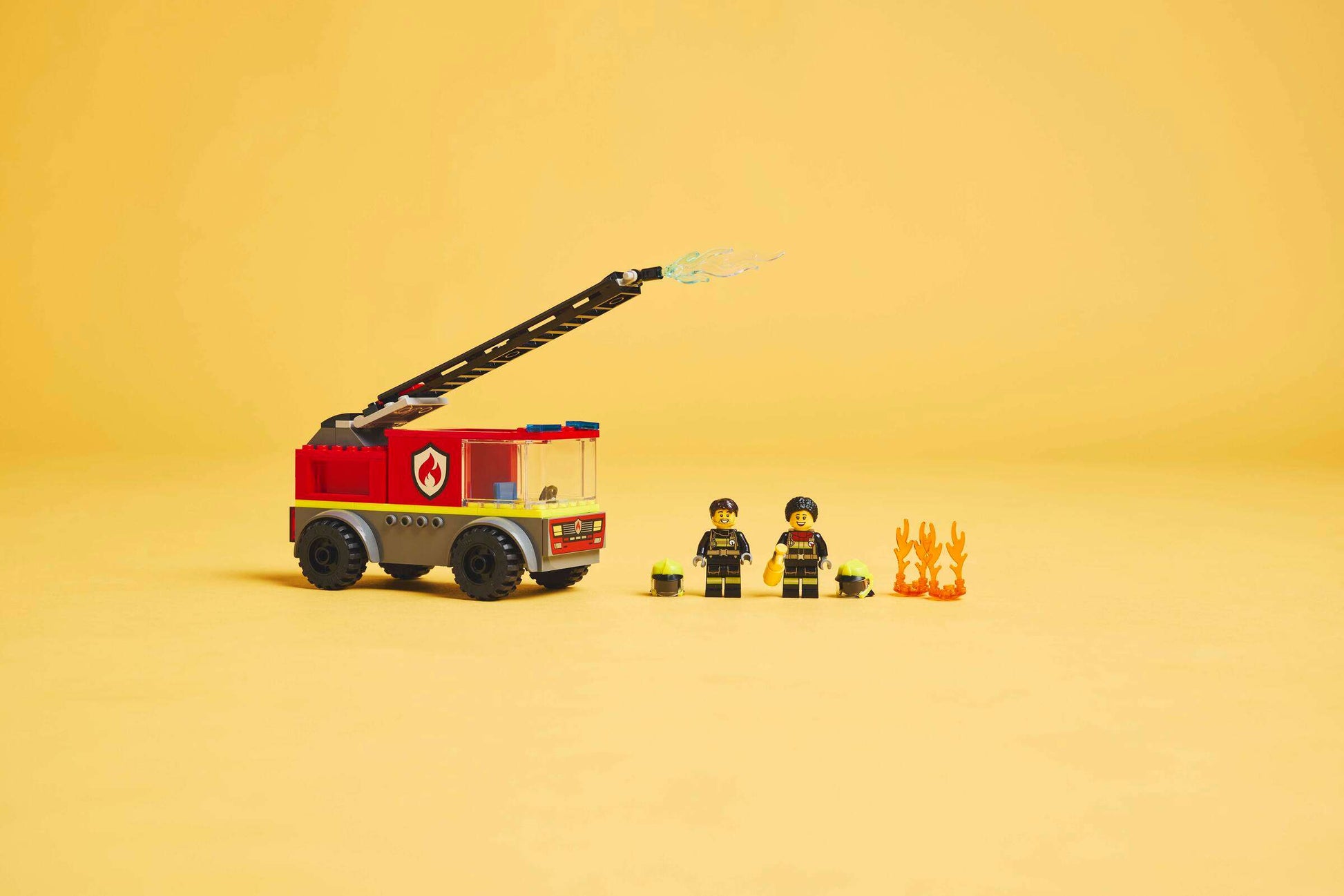 The LEGO® City Fire Ladder Truck by Legos - Toyhouse includes a fire truck with extendable hose, 2 firefighter minifigures, helmets, and LEGO flames, shown on a plain yellow background.