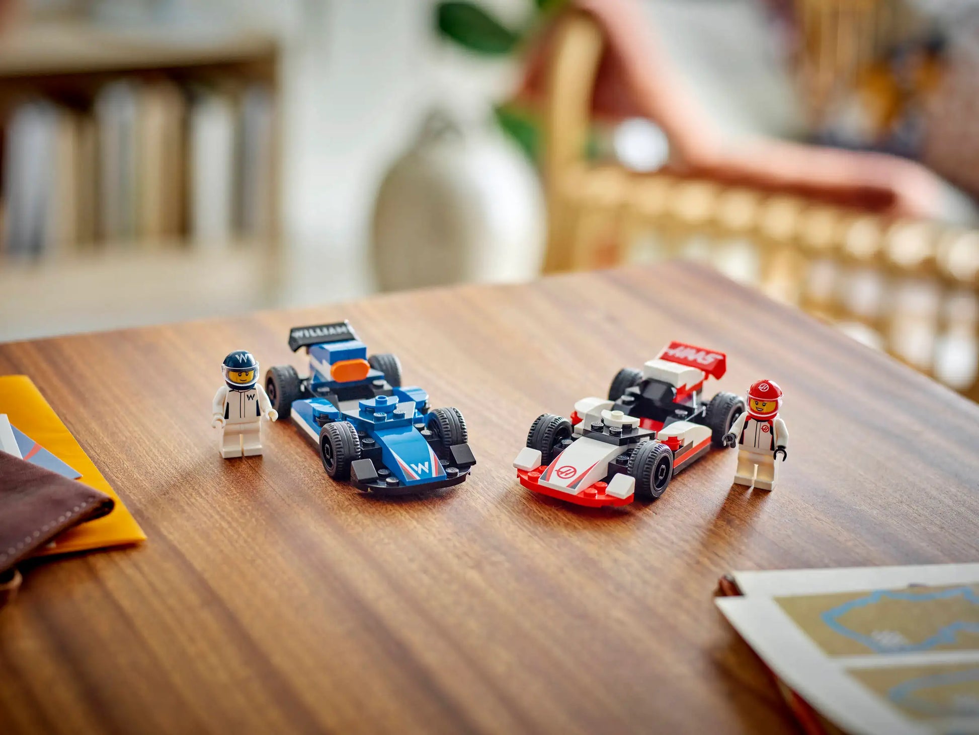 The LEGO® City F1® Williams Racing & Haas F1® Race Cars by Legos - Toyhouse, featuring blue and red/white cars with matching driver minifigures, are displayed on a wooden table.