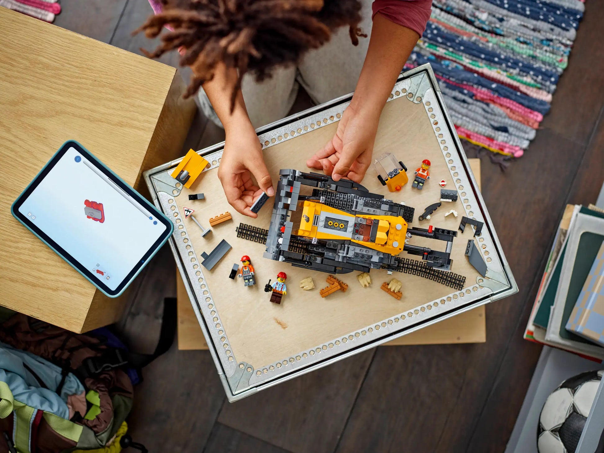 A person assembles the LEGO® City Yellow Bulldozer by Legos - Toyhouse on a tray, with building toy pieces and an iPad showing instructions nearby.