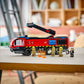 A Legos - Toyhouse LEGO® City Airport Fire Truck with an extending arm is on a table, surrounded by five firefighter minifigures and fire accessories in a brightly lit room.
