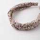 A stylish and comfortable Girls’ Knotted Headband by Rylee & Cru, featuring a twisted knot design with a brown floral pattern on a cream background, is displayed on a white surface.