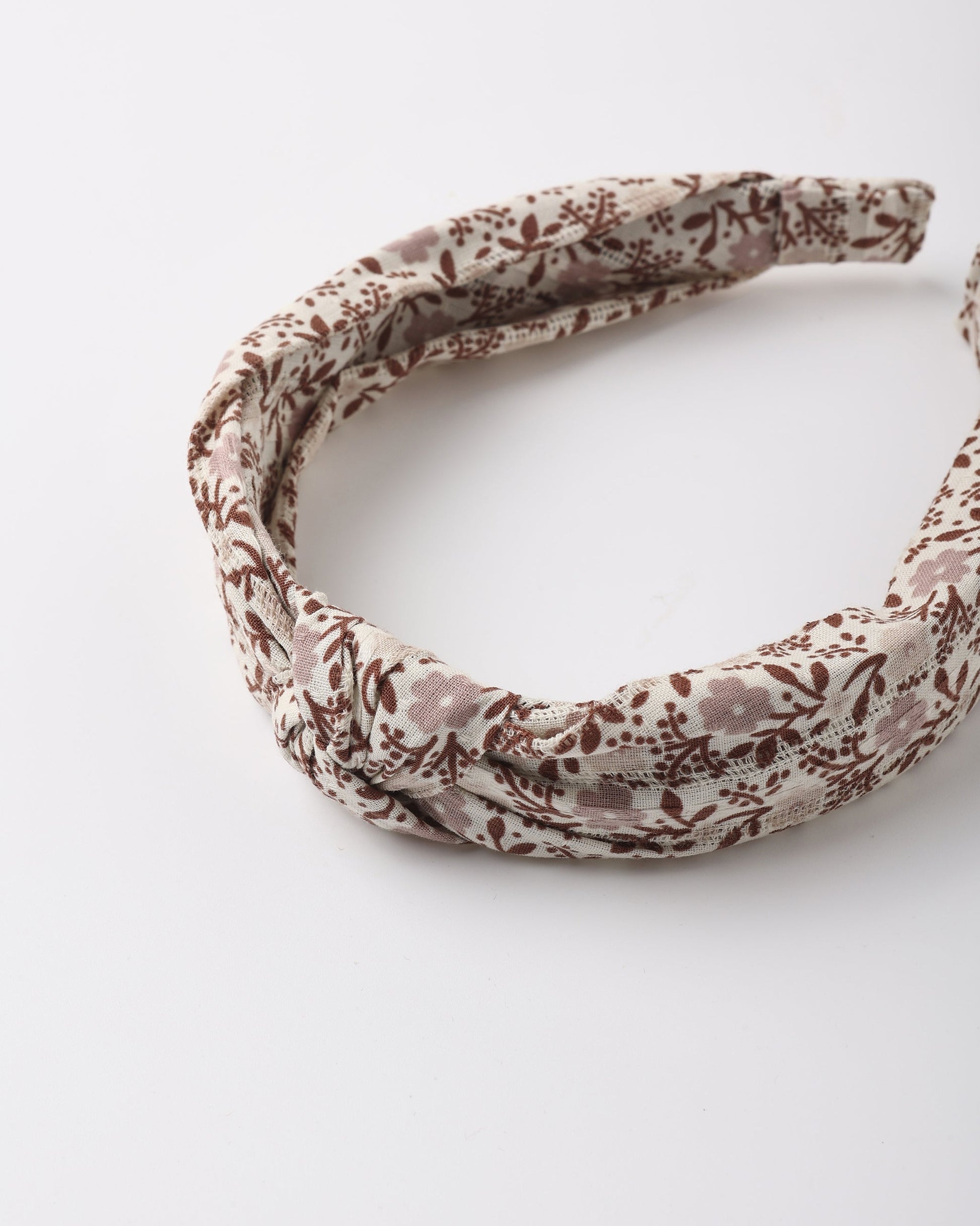 A stylish and comfortable Girls’ Knotted Headband by Rylee & Cru, featuring a twisted knot design with a brown floral pattern on a cream background, is displayed on a white surface.
